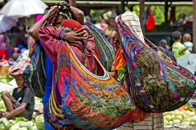 Wanita Papua membawa barang keperluan sehari-hari dengan noken