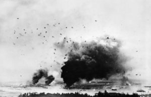 Pemandangan serangan di Pearl Harbour dilihat dari Pearl City. Asap mengepul dan langit dipenuhi puing-puing setelah ledakan di kapal USS Arizona. (Sumber: Imperial War Museums)