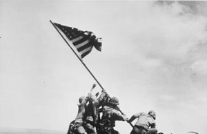 Pasukan Amerika Serikat mengibarkan bendera di puncak Gunung Suribachi selama Pertempuran Iwo Jima. Momen bersejarah itu dipotret oleh fotografer Associated Press Joe Rosenthal. (Sumber: Wikimedia Commons)